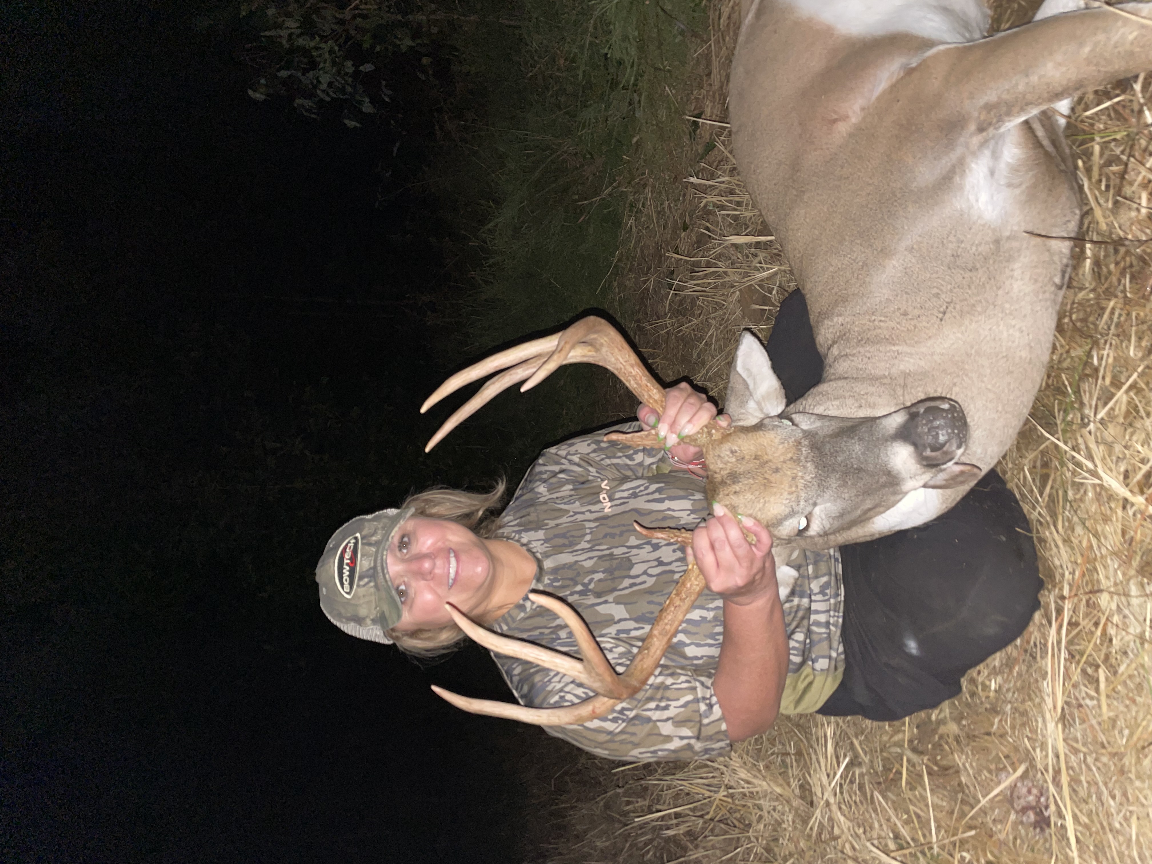 Woman hunter in camouflage with harvested whitetail buck at night