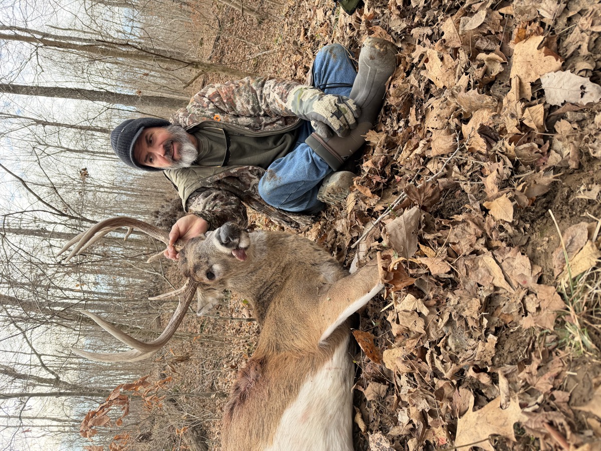 Hunter posing with mature buck in late-season timber