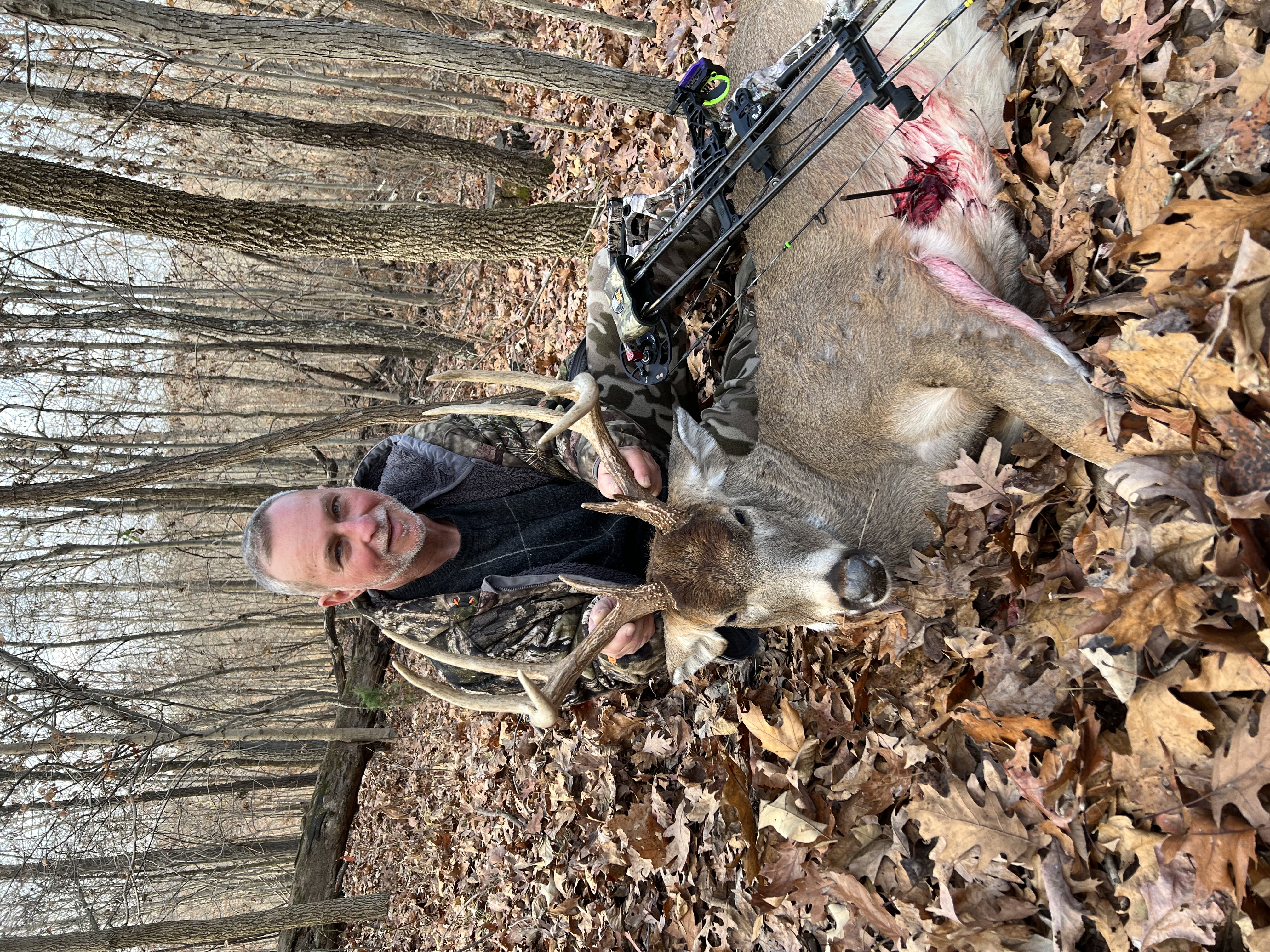 Hunter with harvested whitetail buck and compound bow in wooded Kentucky forest