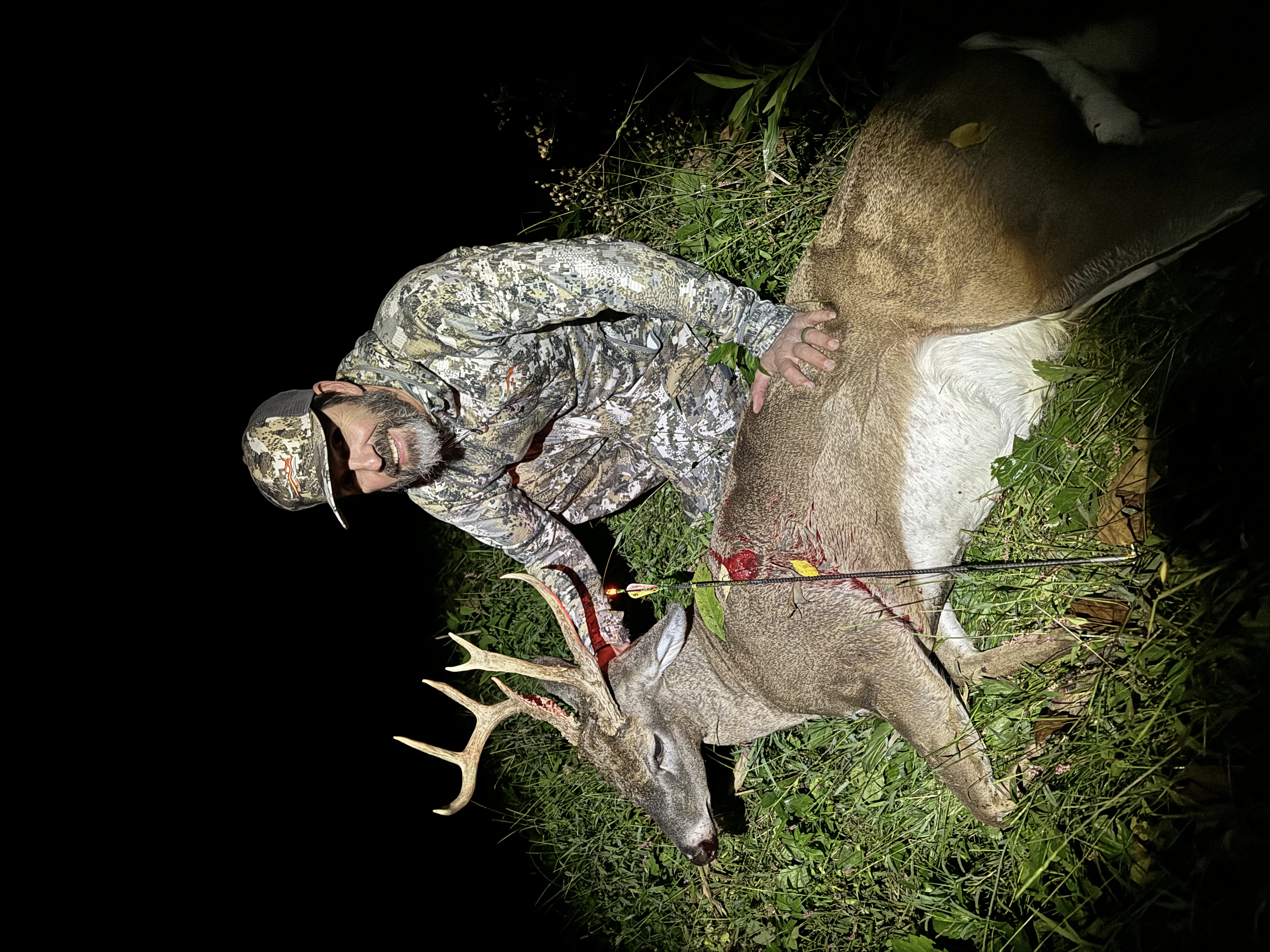 Hunter in camouflage with harvested whitetail buck at night