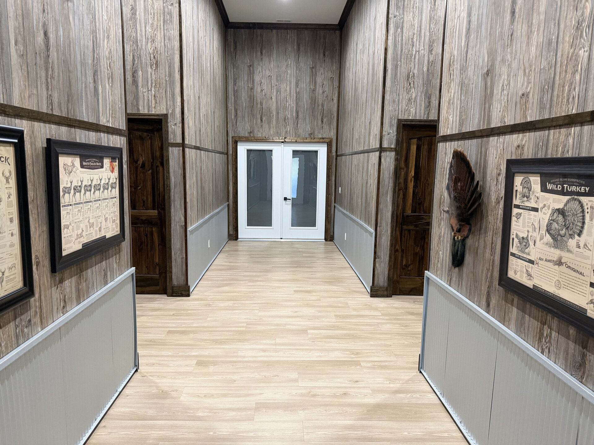Lodge hallway with grey wood paneling, hunting field guides, and a mounted turkey fan